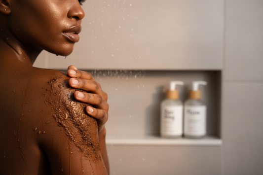 Melanated person applying coffee Scrub to their shoulder in a modern shower, with Zen Mag and Flow bottles on a shelf nearby. Skin glowing, scrub texture visible, soft warm lighting, realistic water droplets, clean minimalistic bathroom background, professional e-commerce style, emphasizing luxury self-care routine.